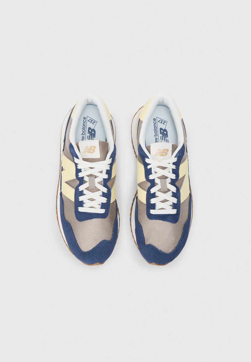 Lichte sneakers met een bovenwerk van mesh in tan en marineblauw, met gele accenten. Witte veters en rubberen zolen maken het ontwerp af.