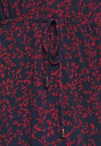Robe en tissu bleu marine avec un motif floral rouge, taille cintrée avec un cordon à nouer, ornée d'accents métalliques sur les cordons.