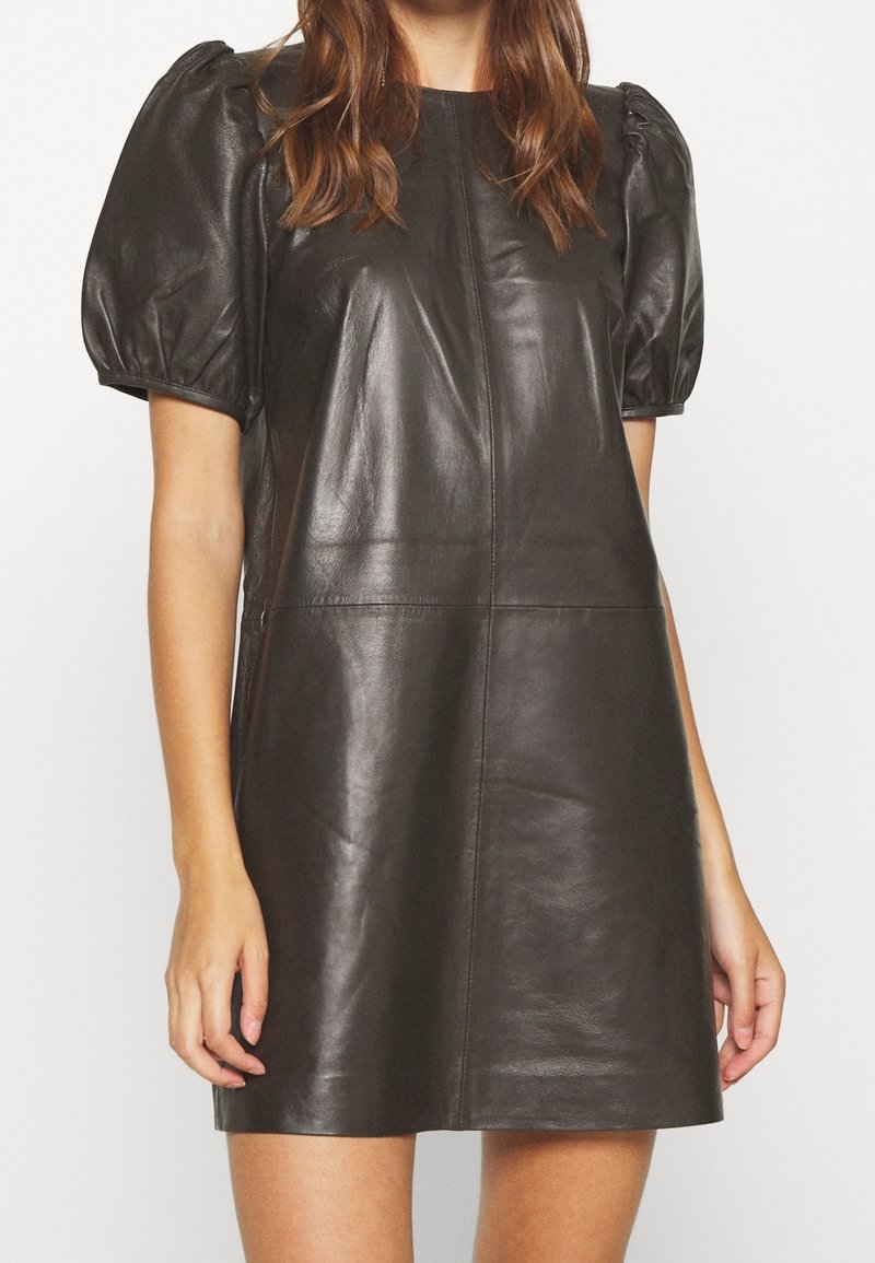 Abito in pelle nera con maniche corte a sbuffo, forma strutturata e design minimalista con cuciture visibili e texture liscia.