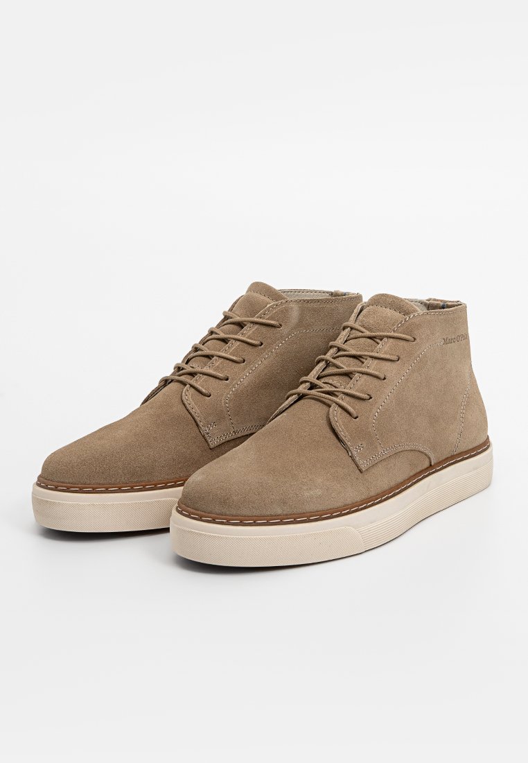 Beige Wildleder Stiefeletten mit runder Zehenpartie, die ein klassisches Schnürdesign, eine tanfarbene Gummisohle und Nähte entlang der Kante aufweisen.