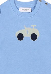 Felpa azzurra chiara con un design di trattore in crema e blu scuro. Presenta bottoncini sulle spalle e polsini e scollatura a coste.