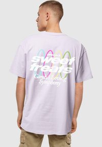 Lavender cotton t-shirt featuring bold white text, "sweet treats," layered with colorful decorative lines. Relaxed fit, crew neck design.