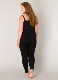 Zwarte playsuit met dunne banden, aansluitend ontwerp, zachte stof en achterzakken. Soepele textuur en lange pijpen.