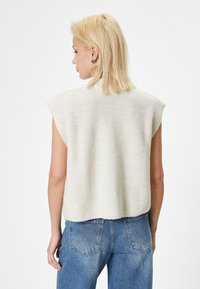 Top senza maniche lavorato a maglia di un leggero color crema, con una texture a coste, caratterizzato da un scollo rotondo e un orlo leggermente asimmetrico, abbinato a jeans di denim.