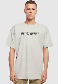 Lys grå oversized t-shirt lavet af bomuld, med en mørk, fed tekstgrafik der står "ER DU BANG?" på brystet.