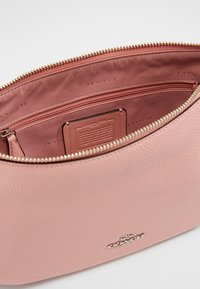 Sac en cuir rose avec une surface texturée, une fermeture éclair dorée et une poche intérieure. Présente le logo de la marque embossé sur un côté.