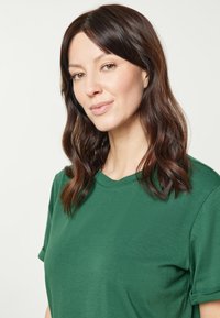 Grön kortärmad t-shirt i ett mjukt, texturerat tyg med rund halsringning och uppvikta ärmslut. Ren, enkel design utan mönster.