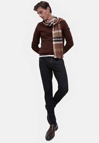 Brun langærmet sweater med et ternet tørklæde, mørke jeans og mørke loafers. Tørklædet har beige, brune og sorte mønstre.