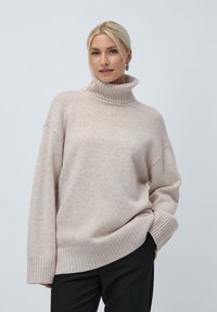 Φωτεινό μπεζ ζακέτα τύπου turtleneck φτιαγμένη από μαλακό πλεκτό ύφασμα. Διαθέτει ριχτές μανσέτες και στρίφωμα, με χαλαρή εφαρμογή και διακριτική λεπτομέρεια λογότυπου.