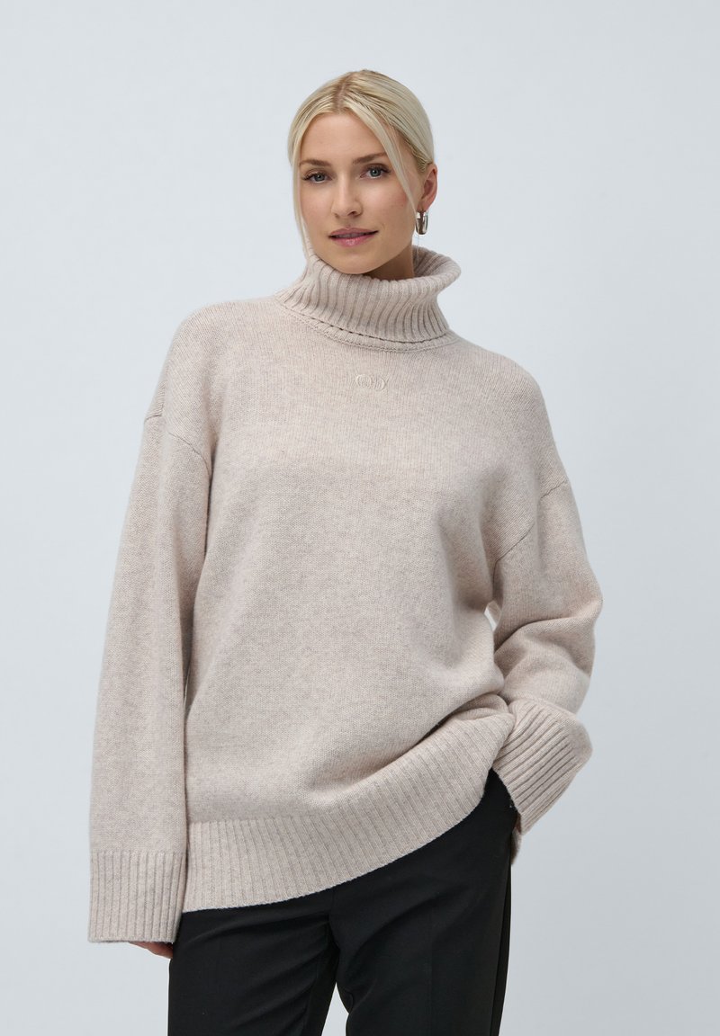 Φωτεινό μπεζ ζακέτα τύπου turtleneck φτιαγμένη από μαλακό πλεκτό ύφασμα. Διαθέτει ριχτές μανσέτες και στρίφωμα, με χαλαρή εφαρμογή και διακριτική λεπτομέρεια λογότυπου.