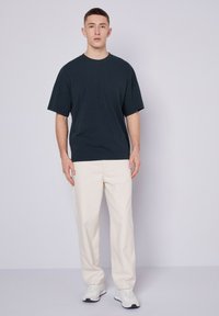 Tamsiai mėlynas oversized trumpomis rankovėmis marškinėliai, derinami su kreminės spalvos tiesiomis kelnėmis ir baltomis sportinėmis bateliais. Lygus audinio tekstūra.