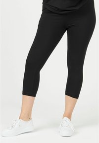 Black 3/4-length leggings made of stretchy fabric with a smooth texture. Paired with white sneakers, featuring a simple design and no visible patterns.