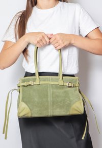 Borsa in suede verde con dettagli in pelle, due manici superiori e una tracolla removibile. Presenta una forma strutturata e legature decorative sui lati.