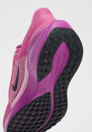 Gros plan sur la semelle d'une basket Nike rose et violette montrant la bande de roulement noire texturée et la tige en mesh avec un swoosh noir.