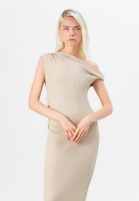 Beige yhden olkapään mekko, joka on valmistettu teksturoidusta kankaasta. Mekossa on drapeerausdesign ja muotoiltu siluetti, jossa on sileä pinta ilman näkyviä koristeluja.