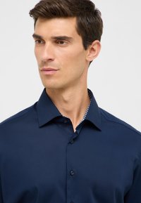 Camicia blu navy realizzata in tessuto liscio, con colletto classico, chiusura a bottoni sottile e rifinitura interna del colletto a contrasto con motivo.