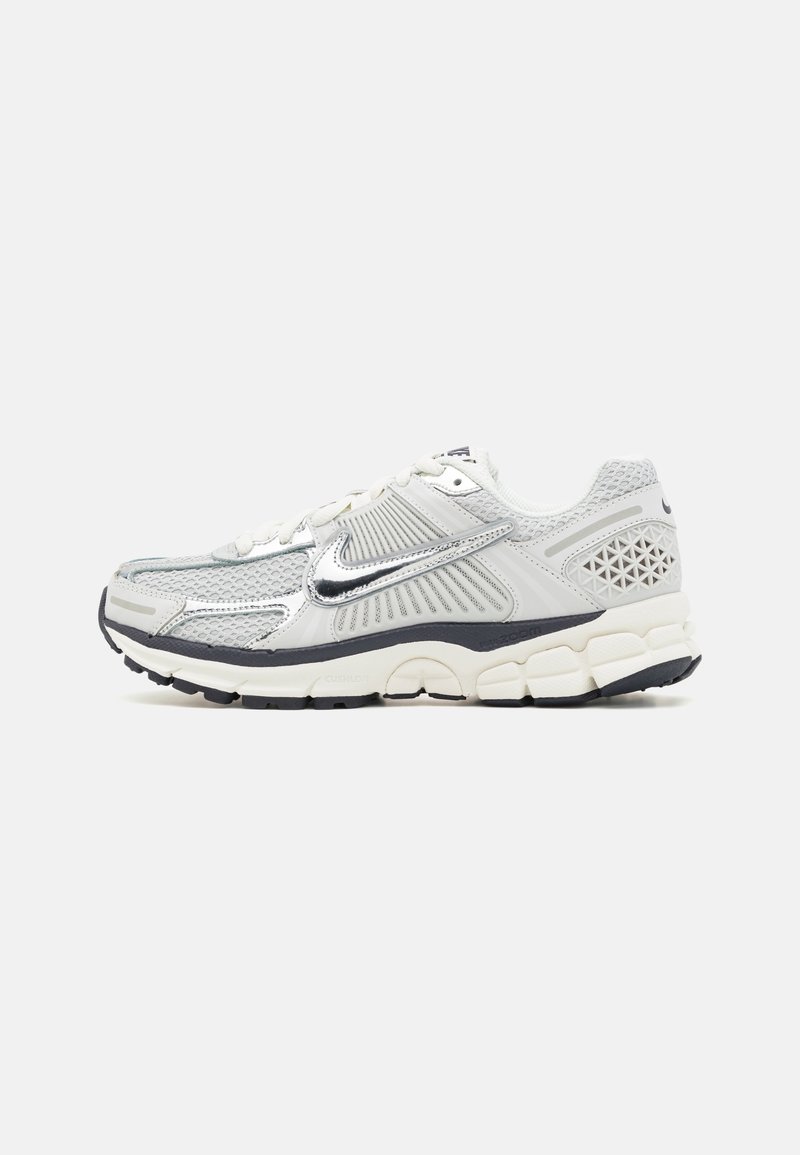 Chaussure de course Nike blanche et grise avec panneaux en mesh, logo Swoosh argenté, semelle rembourrée et semelle extérieure noire, vue de profil.