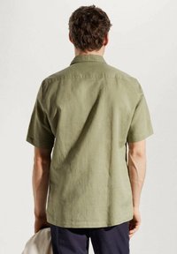 Camisa de manga corta en color verde oliva claro, hecha de tejido texturizado. Cuenta con un cuello estándar y un dobladillo recto, con un ajuste relajado.