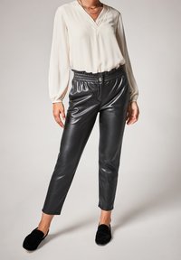 Pantalons en simili cuir noir avec une taille élastique, associés à un chemisier crème avec un décolleté en V et de longues manches bouffantes.