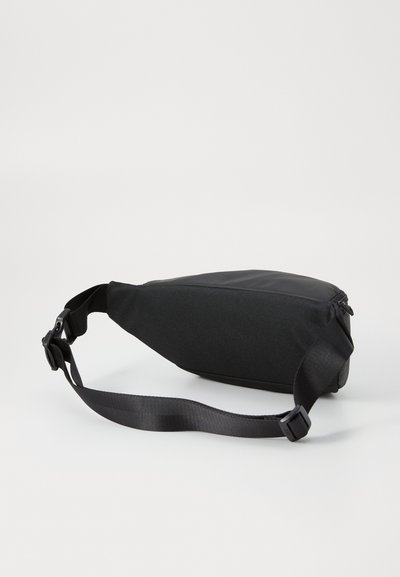 Sac bandoulière noir vu de côté, montrant la sangle réglable et la fermeture éclair. Le sac a un design épuré et minimaliste.