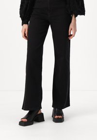 Sorte flared bukser lavet af denim, med høj talje og lige ben design, med kontrastsying, parret med sorte platform sandaler.