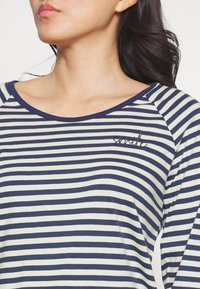 Marineblauwe en crèmewitte gestreepte lange mouwen top met een brede halslijn en geborduurde "smile" details op de borst. Zachte stof met een losse pasvorm.