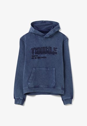 Blauer Kapuzenpullover mit einer Fronttasche. Verfügt über gestickten Text "TROUBLE" und "CREATIVES ARE THE NEW ATHLETES" in kontrastierendem dunklem Faden.