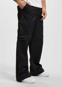 Pantalons cargo noirs à jambes larges, dotés de plusieurs poches et d'un tissu lisse et durable. Portés avec des baskets blanches.