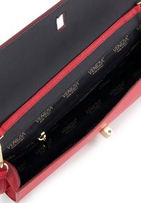 Rood leren handtas met een zwarte binnenzijde. Beschikt over gouden hardware, een ritsvak en een textuur buitenkant. Logo-patroon voering zichtbaar.