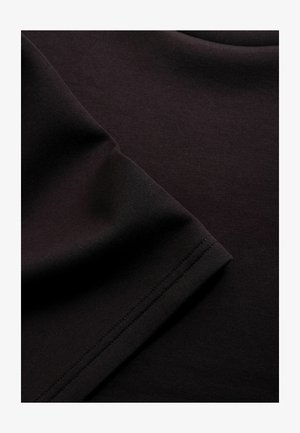 Nærbillede af sort stof foldet med synligt søm på kanten, der viser glat tekstur og fine vævedetaljer.