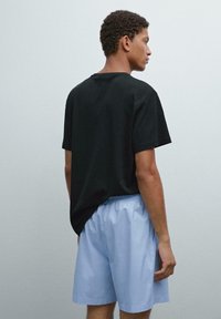 Zwarte katoenen t-shirt met een ontspannen pasvorm, gecombineerd met lichtblauwe shorts met een elastische tailleband en zijzakken. Effen achtergrond.