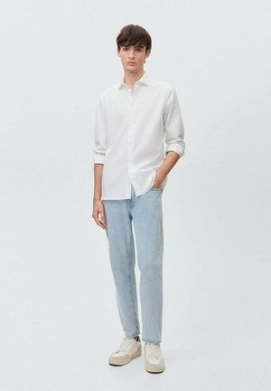 Biała koszula z długim rękawem i zapięciem na guziki, jasnoniebieskie proste dżinsy oraz beżowe sneakersy. Minimalistyczny styl i miękka tekstura.