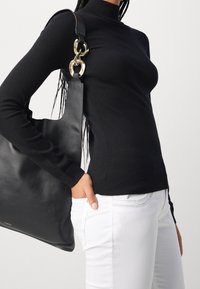 Zwarte getailleerde coltrui gecombineerd met witte jeans. Een grote zwarte leren tote bag met een gouden hardware accent op de schouderband.