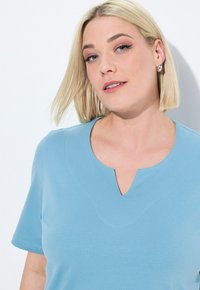 Světle modrý krátký rukáv top s výstřihem do V a jemným texturovaným prošíváním. Měkká tkanina s uvolněným střihem.