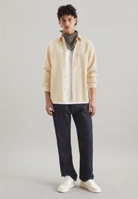 Light yellow textured button-up shirt over a white t-shirt, paired with dark denim jeans and white sneakers, accessorized with a patterned scarf.