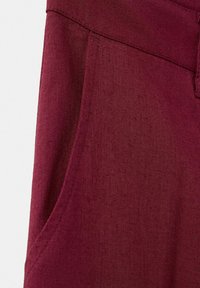 Gros plan sur la poche d'un pantalon en lin bordeaux, montrant la texture du tissu et les détails des coutures.