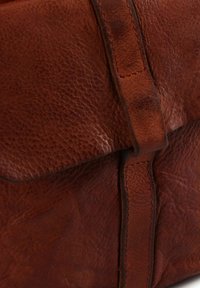 Bruine lederen tas met een gestructureerde afwerking, voorzien van een klep met sluiting en gestikte accenten langs de randen. Compact, rechthoekig model.