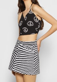Černý crop top s potiskem mírového symbolu v kombinaci s černobílou kostkovanou mini sukní, která má rovný střih a boční kapsy.