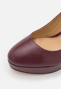 Zbliżenie na damskie buty na platformie z bordowej skóry, o zaokrąglonym nosku i beżowej wyściółce wewnętrznej.