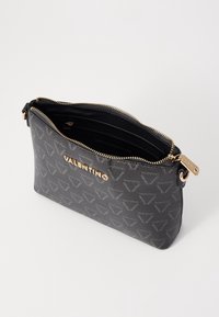 Czarna torebka ze skóry o fakturze, z złotym logo, zamkiem błyskawicznym oraz wnętrzem podzielonym na kilka przegródek. Zewnętrzna powierzchnia ozdobiona wzorem.