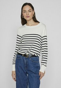 Jersey de manga larga a rayas en blanco y negro, confeccionado en suave tejido de punto, combinado con vaqueros de mezclilla azul de cintura alta y un cinturón negro.