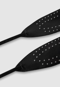 Czarne skórzane paski butów z srebrnymi ćwiekami ułożonymi w wzór, charakteryzujące się gładką teksturą i spiczastym kształtem, przymocowane cienkimi paskami.