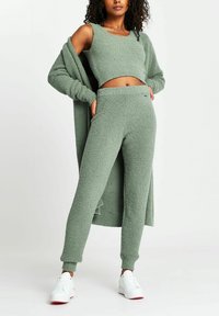 Set di loungewear in fleece verde oliva, con texture, composto da un top corto, pantaloni a vita alta e un cardigan lungo, abbinato a sneakers bianche.