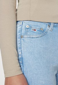 Jeans de mezclilla azul claro con una textura deslavada, que presentan herrajes plateados y un pequeño logo rojo, blanco y azul en el bolsillo frontal.