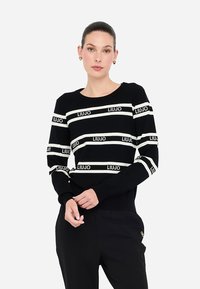 Maglione a righe bianco e nero, in morbido tessuto a maglia, con il marchio "LIU JO". Collo rotondo e vestibilità rilassata con spalle scese.