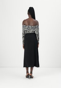 Off-shoulder topp med zebra mønster i svart og hvitt, kombinert med et langt svart skjørt. Har strukturert stoff og tettsittende midje.