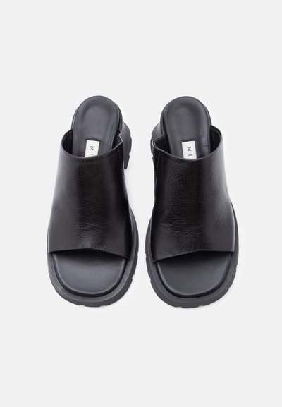 Ζευγάρι μαύρα δερμάτινα σανδάλια με ανοιχτά δάχτυλα, χωρίς λουράκι, με χοντρές λουρίδες και μαξιλαρωμένες σόλες σε απλό ανοιχτό φόντο.
