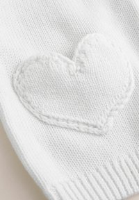 Bela pletenina z teksturirano obliko srca, z ribastimi robovi in izšitim obrisom, ki prikazuje mehak, prijeten material.