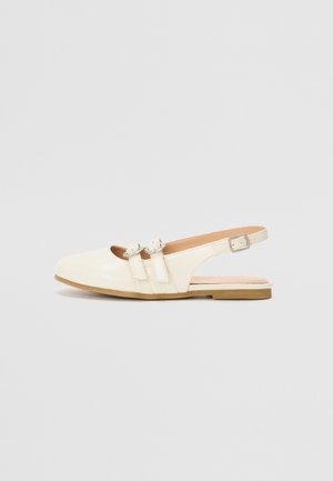 Kremowe płaskie sandały typu slingback z dwoma paskami zapinanymi na klamry i zaokrąglonym zamkniętym noskiem na jasnym tle.