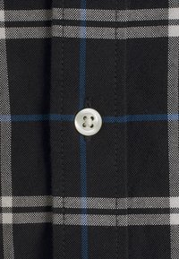 Zwarte katoenen shirt met een ruitpatroon met witte en blauwe lijnen, en een witte knop bij de kraag. Getextureerde stof met zichtbare stiksels.